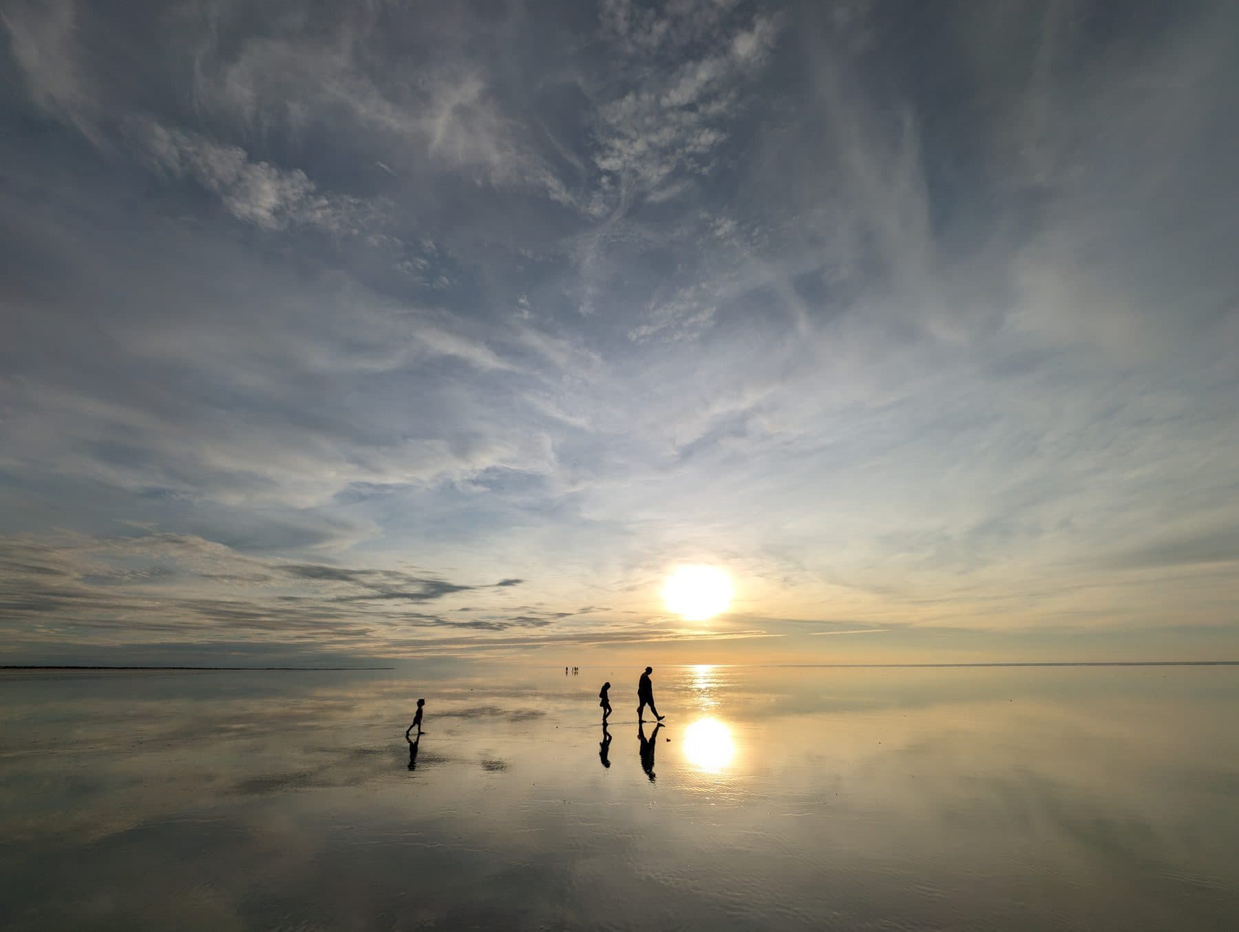 Walkers silhouetted on the mirror-flat sands of 80 Mile Beach at sunset