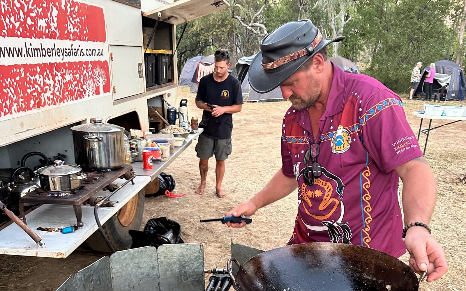 Guide Jason cooking dinner on the camp kitchen wok beside the Kimberley Safari Tours truck at Bell Gorge, with guide Jesse behind him